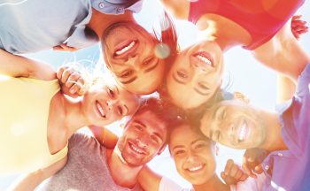 Stock image of young people, viewed from below, with their arms linked in a circle, smiling