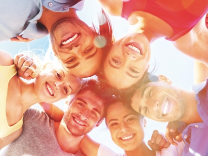 Stock image of young people, viewed from below, with their arms linked in a circle, smiling