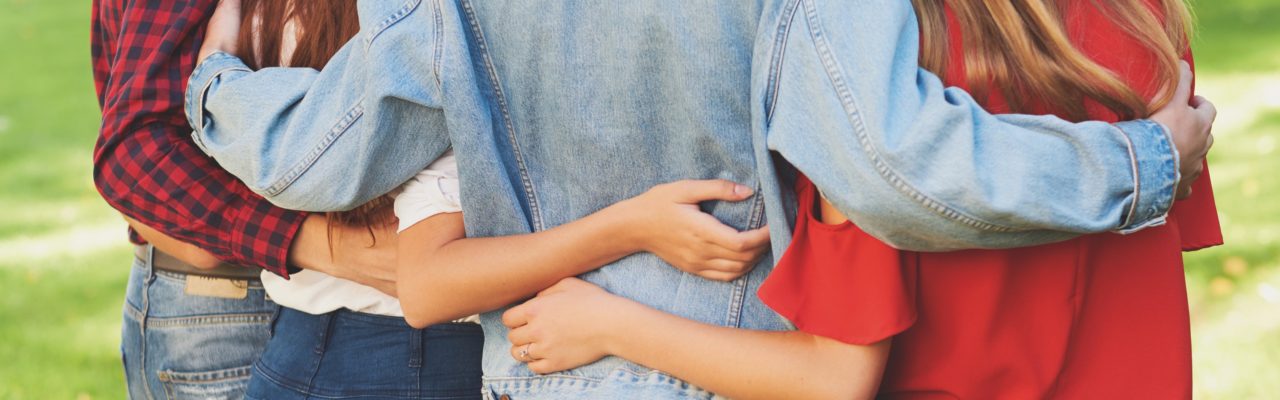 Stock image of young people from behind, displaying their arms linked around each others' shoulders and waists