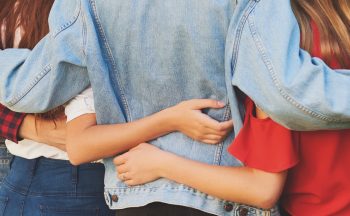 Stock image of young people from behind, displaying their arms linked around each others' shoulders and waists