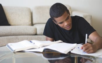 Stock image of a teenage boy doing homework at a living room table