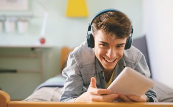 Stock image of a teenage boy smiling and listening to music in his bedroom