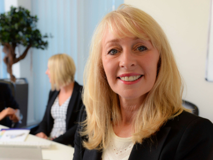 Photograph of Julie Stirpe in a corporate boardroom, with other professionals in the background