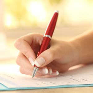 Stock photo in extreme close up of a hand filling out paperwork with a red pen